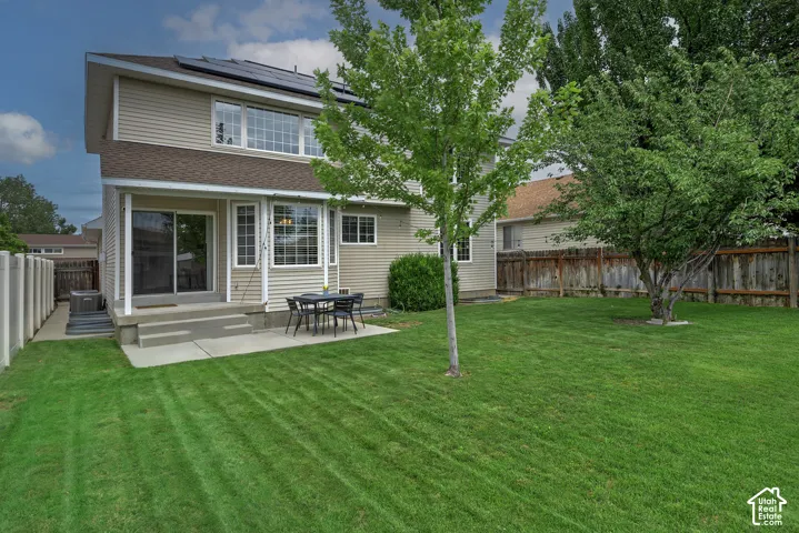 Expansive rear lawn with mature trees, a concrete patio, and a covered back porch with a sliding glass door