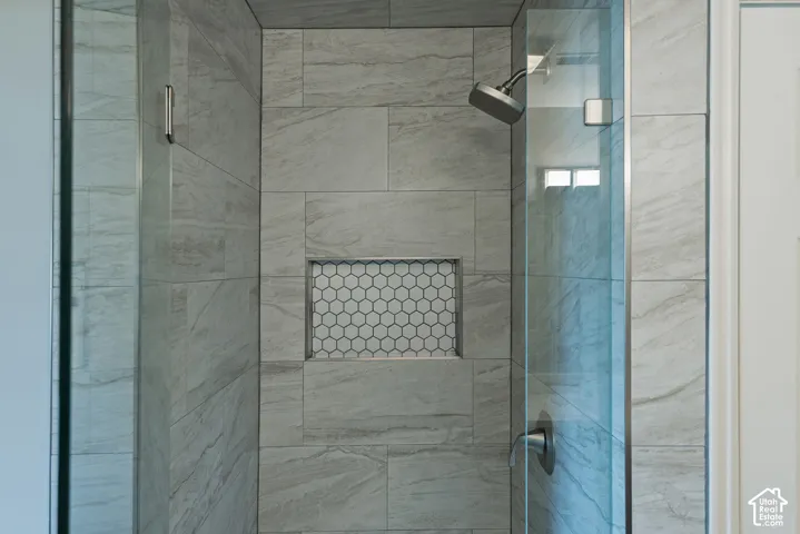 Glass-enclosed shower with large format tile surround, a built-in hexagonal tile niche, and a brushed nickel showerhead
