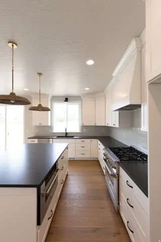 Kitchen featuring white cabinetry, dark countertops, wood-finish flooring, stainless steel appliances, and pendant lighting