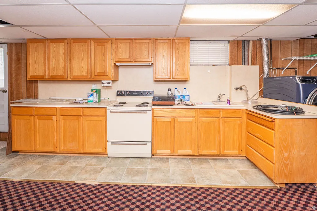 Kitchenette area featuring wood-finish cabinetry, a drop ceiling with integrated lighting, a built-in range, and a sink with a faucet