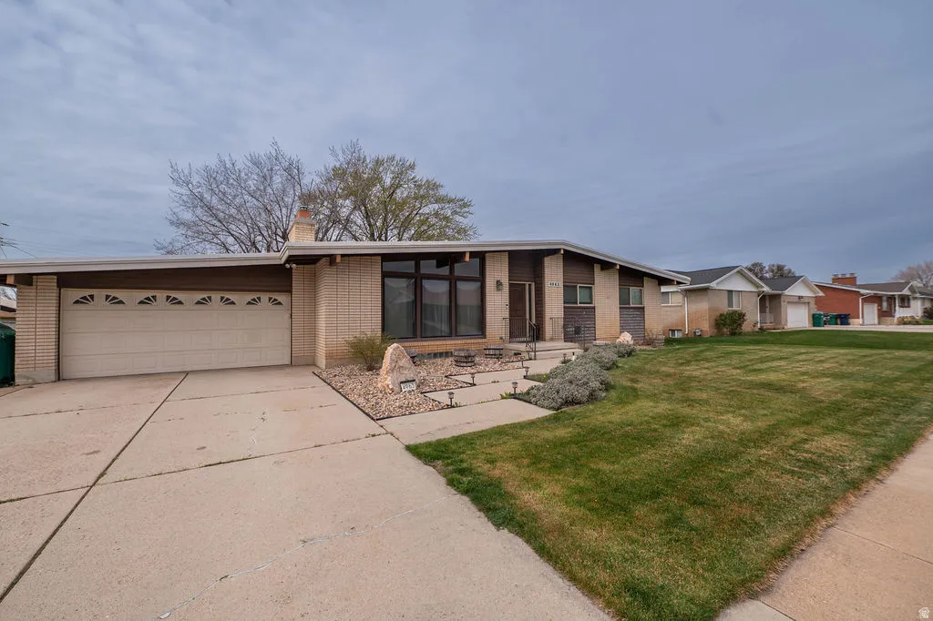 Mid-century modern exterior featuring a low-pitch roofline, brick and wood-panel accents, an attached two-car garage, and a concrete driveway