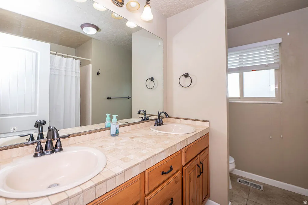 Double vanity with tile countertop, oil-rubbed bronze fixtures, and warm wood-finish cabinetry
