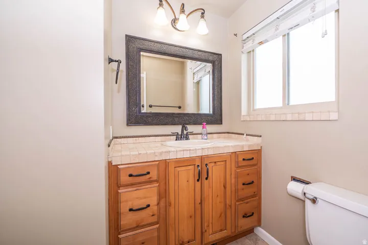 Wood-finish vanity with ample storage, tiled countertop, and framed mirror