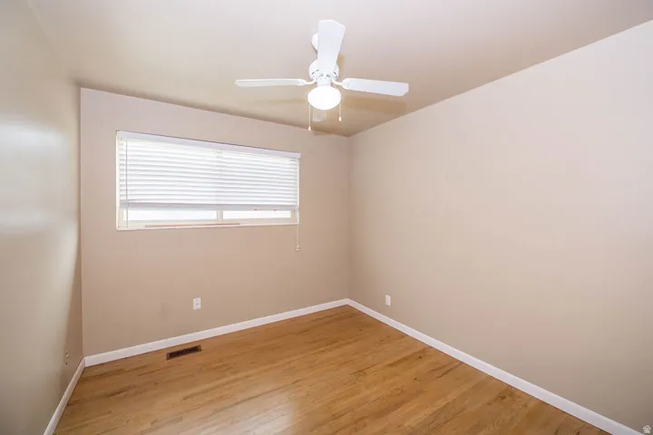 Wood-finish flooring, neutral wall tones, window with horizontal blinds, and a ceiling fan with integrated lighting