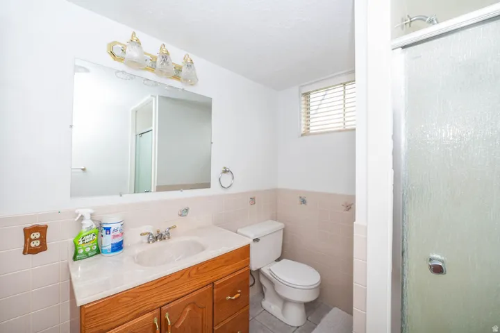 Bathroom featuring a light wood-finish vanity, a framed mirror, a three-light fixture, and a tiled shower enclosure with a clear glass door