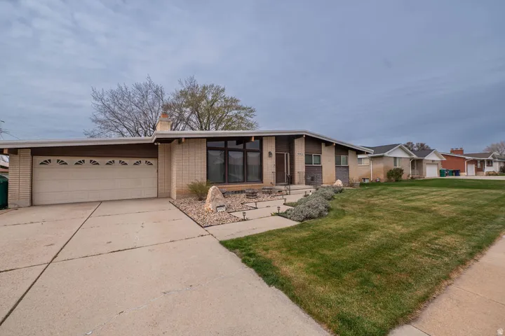 Mid-century modern exterior featuring a low-pitch roofline, brick and wood-panel accents, an attached two-car garage, and a concrete driveway