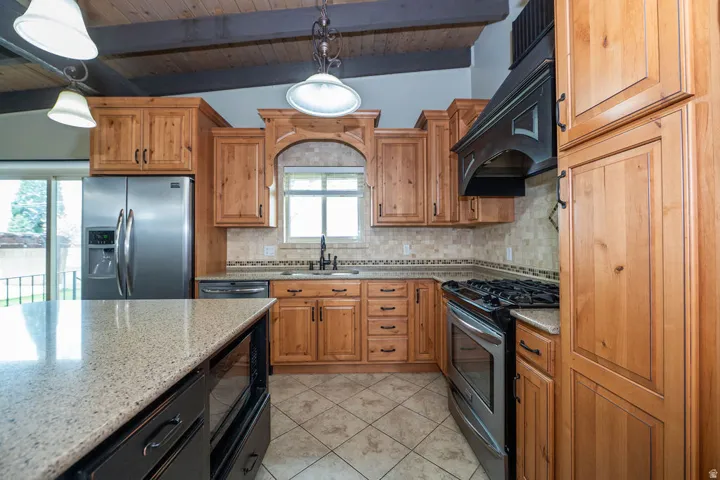 Kitchen featuring wood cabinetry, stainless steel appliances, a tile backsplash, and a large island with a light-toned countertop