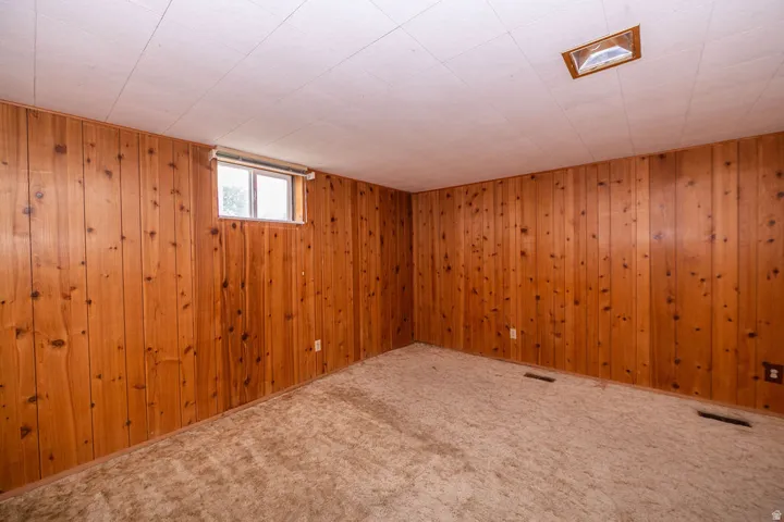Wood-paneled walls with a single window, recessed ceiling light, and carpeted flooring