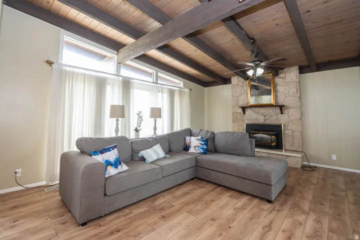 Vaulted wood-paneled ceiling with exposed beams, wood-finish flooring, stone fireplace, and expansive windows