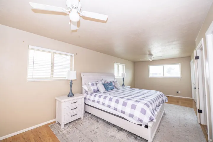 Wood-finish flooring, multiple windows with blinds, ceiling fan, and two interior doors