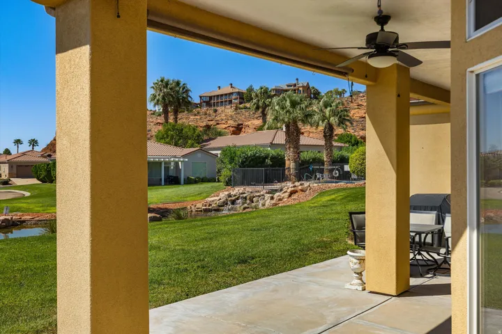 Covered patio with a ceiling fan, concrete flooring, manicured lawn, water feature, and mature palm trees
