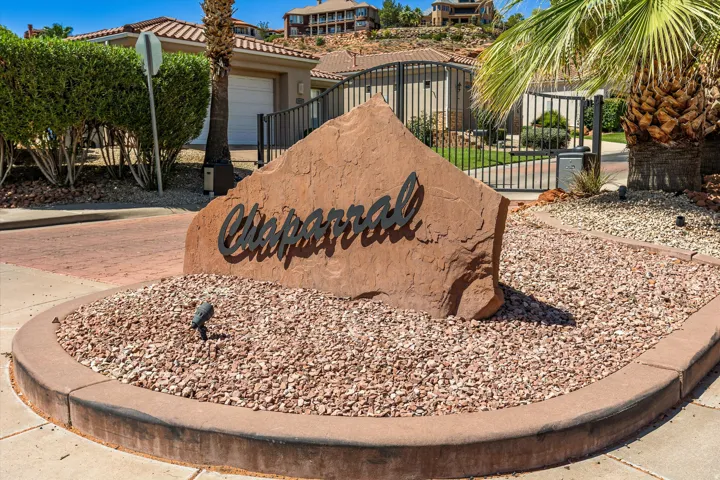 Decorative stone entrance monument, black wrought iron gate, paver driveway, mature palm trees, and manicured landscaping