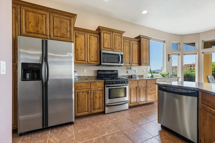 Kitchen featuring wood cabinetry, stainless steel appliances, granite countertops, and tiled flooring
