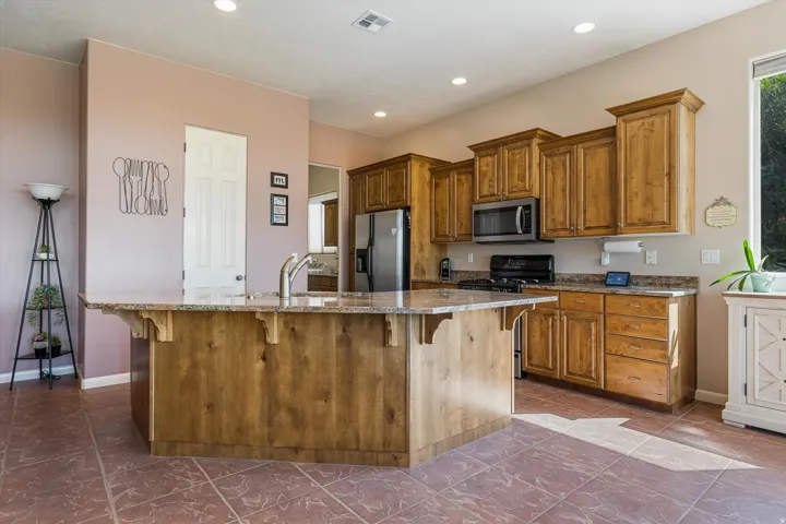 Kitchen featuring wood cabinetry, stainless steel appliances, a center island with sink, and tile flooring
