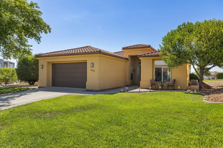 Stucco exterior with a tile roof, an integrated garage, a concrete driveway, a manicured lawn, and mature trees