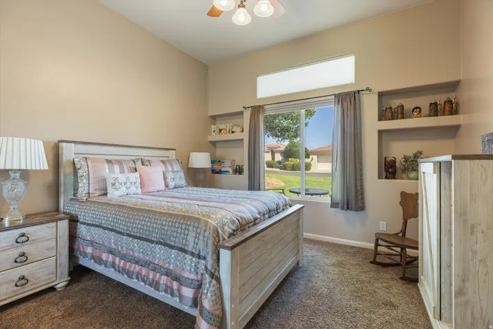 Vaulted ceiling bedroom with built-in wall shelving, a large window, and a transom window above