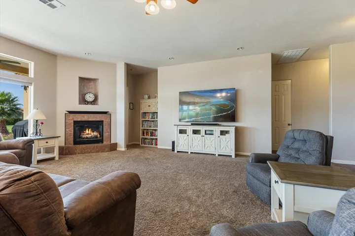 Carpeted living area featuring a corner fireplace with a tiled surround and mantel, a built-in wall niche, and a large window overlooking exterior landscaping