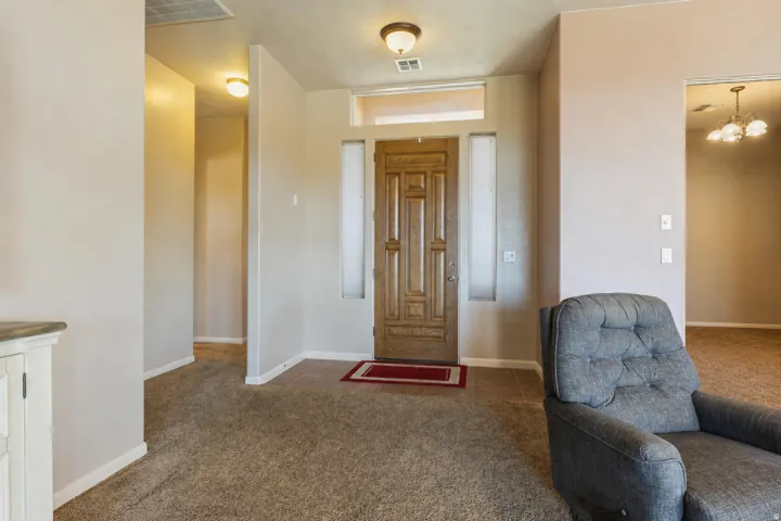 Carpeted flooring throughout, recessed entryway with tile flooring, wood-paneled entry door with sidelights, and a transom window
