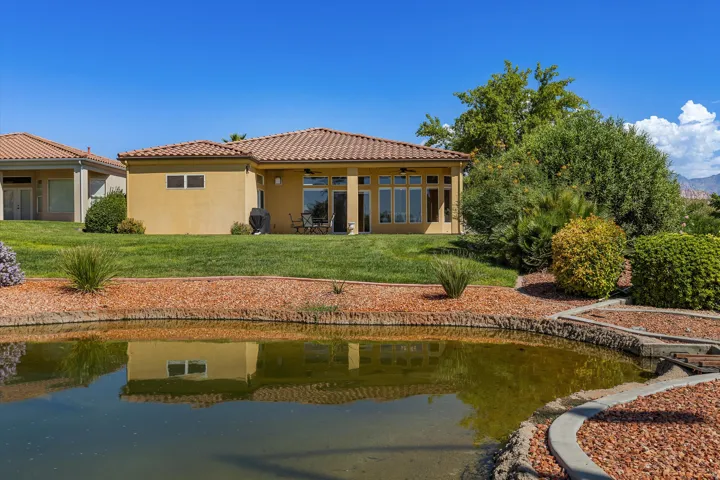 Stucco exterior with a tiled roof, expansive green lawn, mature landscaping, and a tranquil water feature
