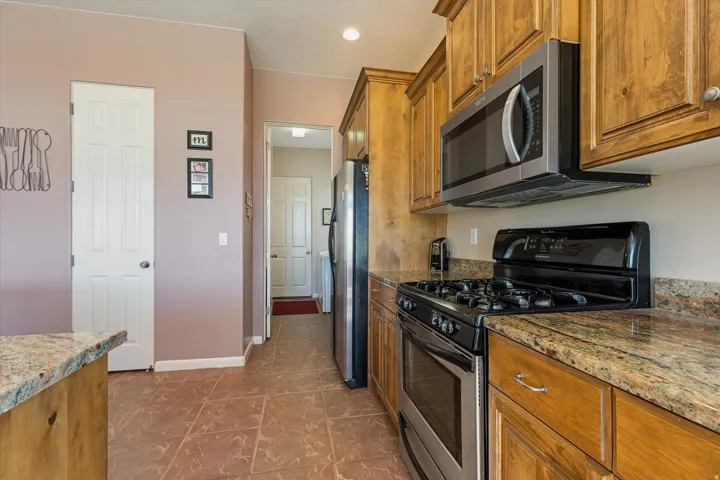 Kitchen featuring wood cabinetry, stainless steel appliances, speckled countertops, and tile flooring