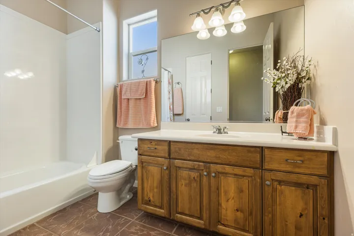 Tile flooring, wood-finish vanity with ample storage, integrated single-basin sink, large wall-mounted mirror, and a full bathtub with shower