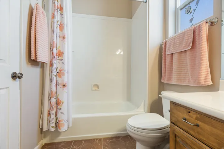 Tub-shower combination with integrated soap dish, toilet, wood-finish vanity with drawer, and tile flooring