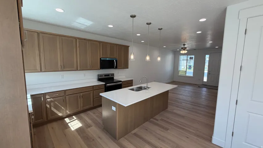 Kitchen featuring light wood-finish cabinetry, white countertops, stainless steel appliances, and a central island with pendant lighting