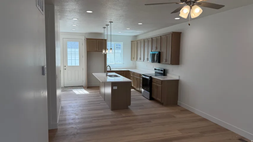 Kitchen featuring wood-finish flooring, recessed lighting, a central island with pendant lighting, and stainless steel appliances