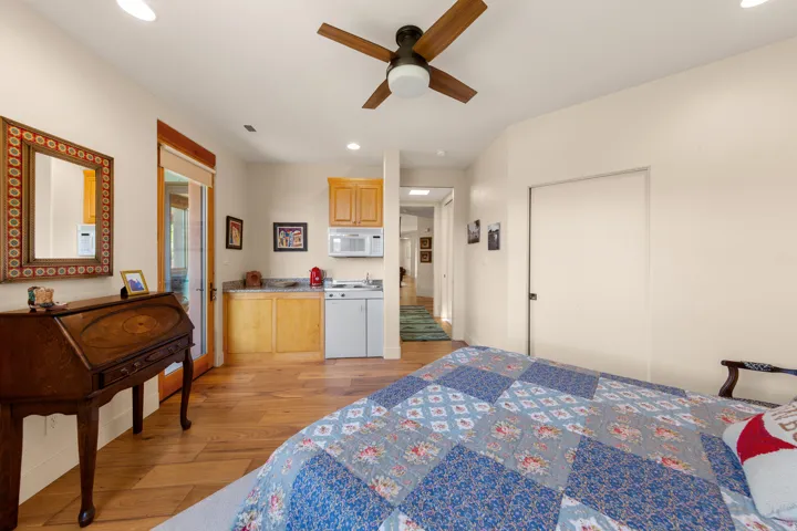 Wood-finish flooring, built-in kitchenette with microwave and cooktop, wood cabinetry, and a ceiling fan with integrated lighting