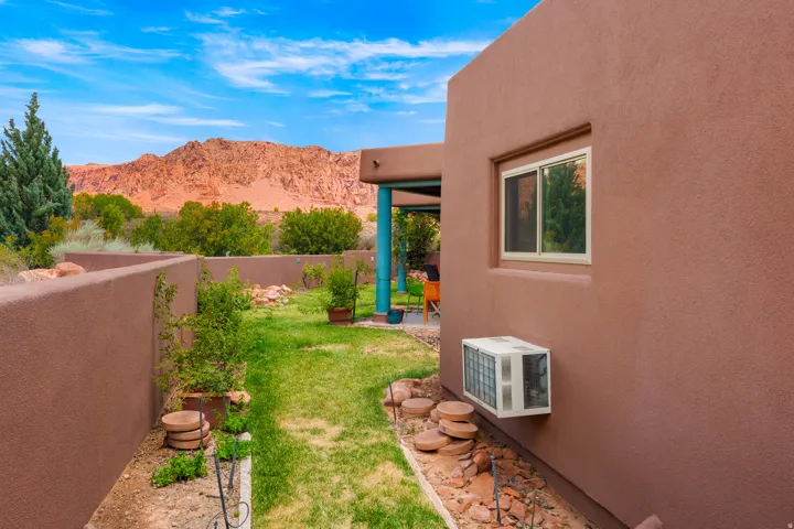 Stucco exterior with a single-pane sliding window, mature landscaping, and a red rock mountain backdrop