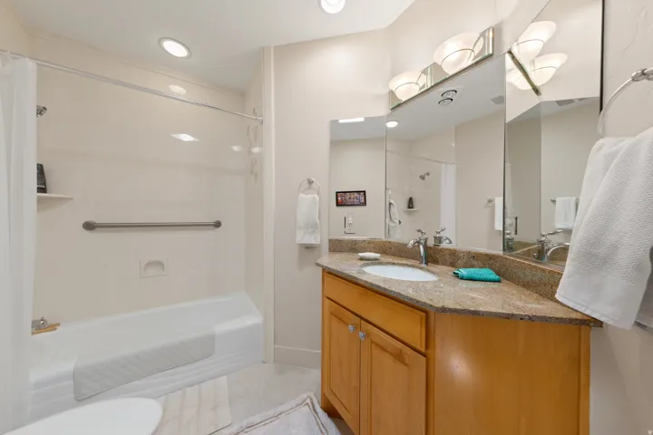 Tile flooring, vanity with light wood-finish cabinetry, stone countertop, integrated sink, and tub with shower
