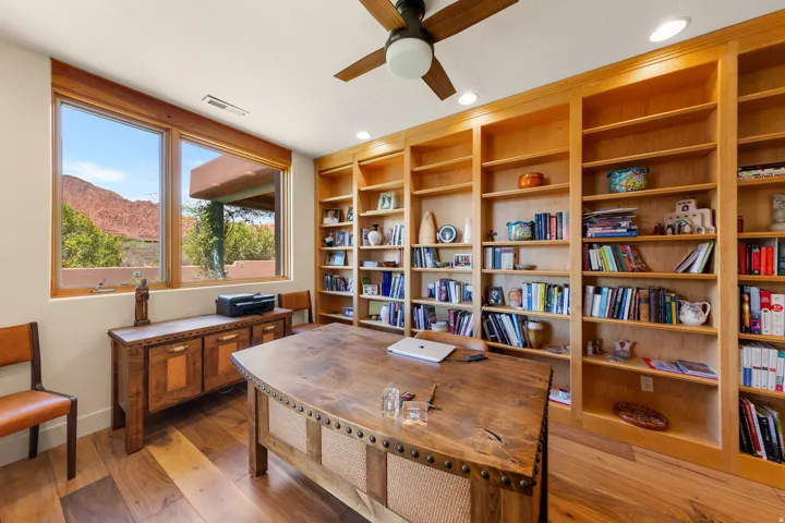 Built-in wood shelving, wood-finish flooring, recessed lighting, ceiling fan, and large windows with wood framing