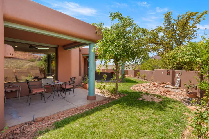 Covered patio with a concrete surface, expansive windows, stucco exterior, and a manicured lawn with established trees