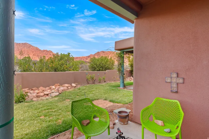 Covered patio with an exterior stucco wall, a manicured lawn, and a desert rock garden