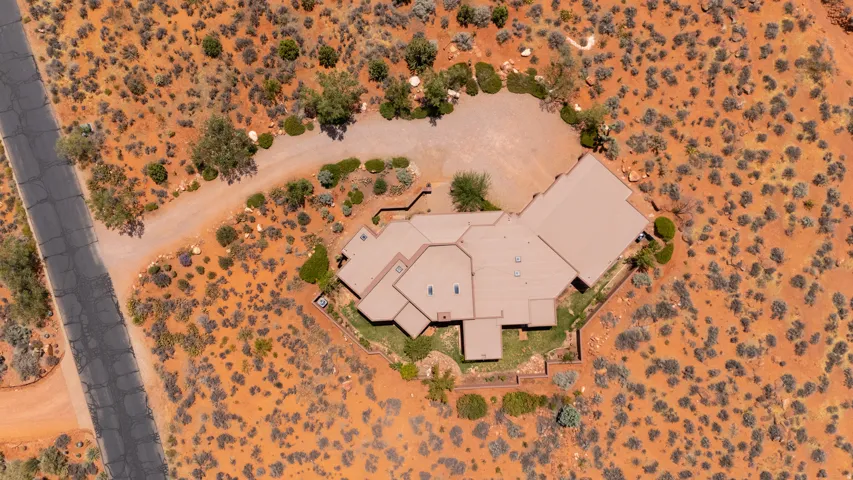 Extensive desert landscaping surrounding a multi-level residence with a private driveway, bordered by a paved road