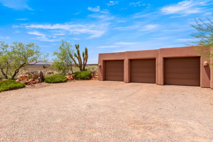 Three-car garage with a stucco exterior, gravel driveway, and desert landscaping