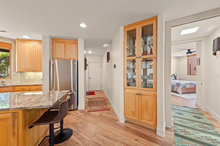 Wood-finish flooring throughout, stainless steel refrigerator, kitchen with granite-finish countertop, wood cabinetry with glass-front display, and recessed lighting