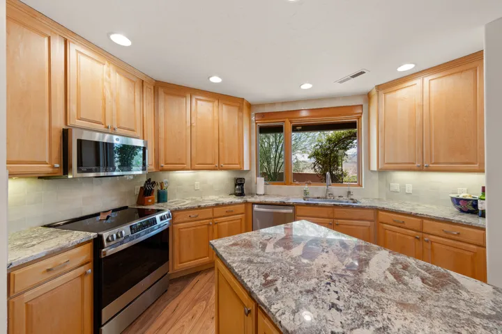 Warm wood cabinetry frames this kitchen, featuring stainless steel appliances, granite-finish countertops, recessed lighting, and a large center island with seating