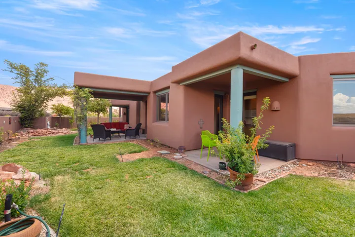 Expansive grass area with a covered patio, shaded outdoor living space, stucco exterior, and integrated outdoor lighting