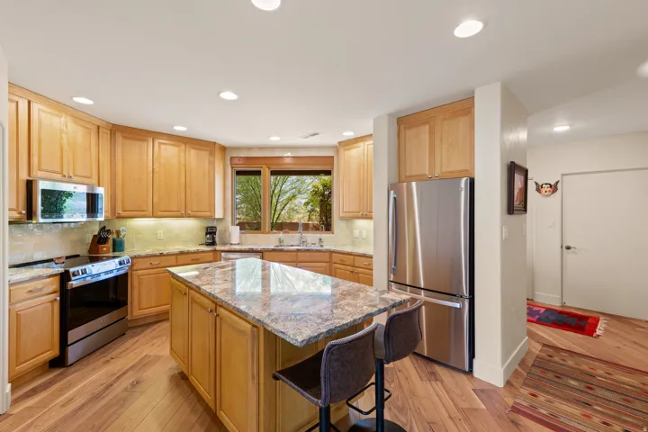 Kitchen featuring wood-finish flooring, recessed lighting, wood cabinetry, stone countertops, and stainless steel appliances