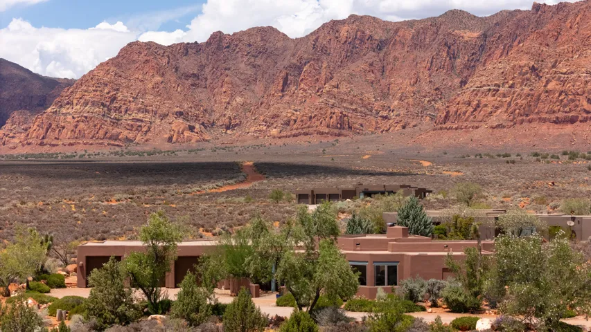Terraced desert landscaping, stucco exterior, multiple window features, mature trees, and a mountain backdrop