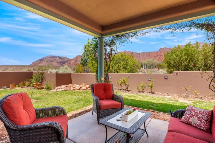 Covered patio with concrete flooring, stucco privacy wall, and manicured lawn