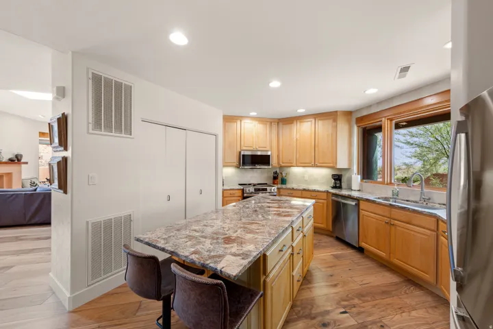 Kitchen featuring wood-finish flooring, an expansive island with a stone countertop, light wood cabinetry, recessed lighting, and stainless steel appliances
