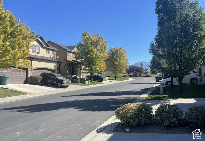 Stucco exterior with arched garage door, concrete driveway, established trees, and mountain backdrop