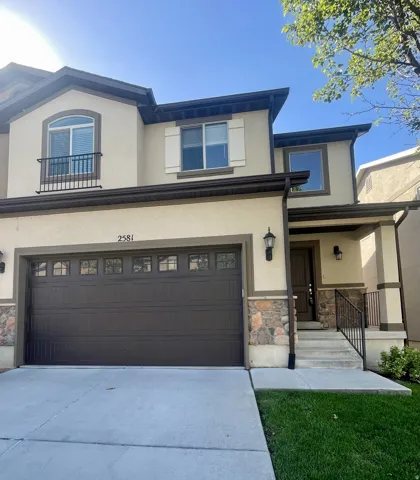 Stucco exterior with stone accents, covered entry porch, dark wood-finish garage door with upper window inserts, and iron balcony railing