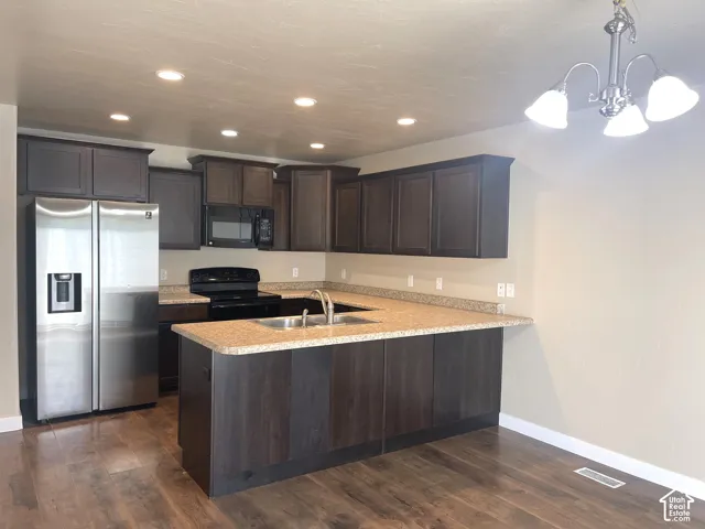 U-shaped kitchen with dark wood-finish cabinetry, light speckled countertops, stainless steel side-by-side refrigerator, and wood-finish flooring