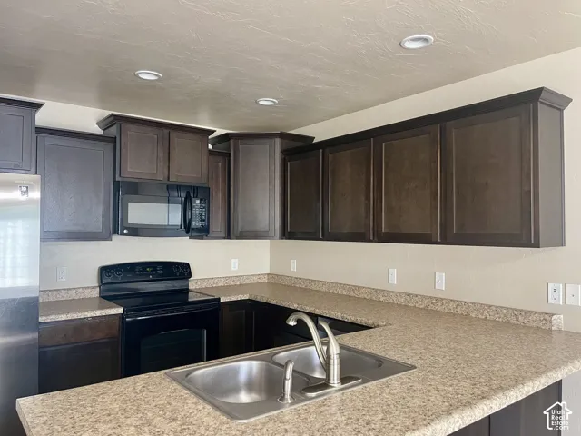 U-shaped kitchen featuring dark wood cabinetry, integrated microwave, black electric range, dual-basin stainless steel sink, and speckled countertops