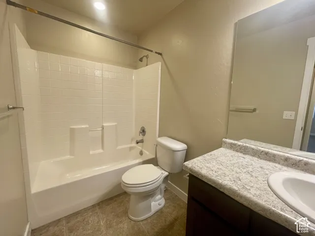 White bathtub and shower combination with tile-look surround, chrome fixtures, dark wood-finish vanity, light speckled countertop, and tiled flooring