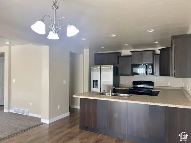 Kitchen featuring dark wood-finish cabinetry, stainless steel refrigerator, black range, and an island with an integrated sink and light-toned countertop