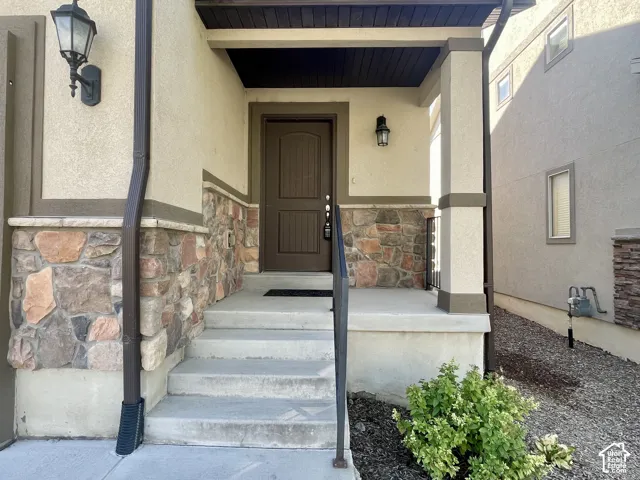 Inviting entryway featuring a covered porch, stone accent siding, concrete steps, and a dark wood-finish door